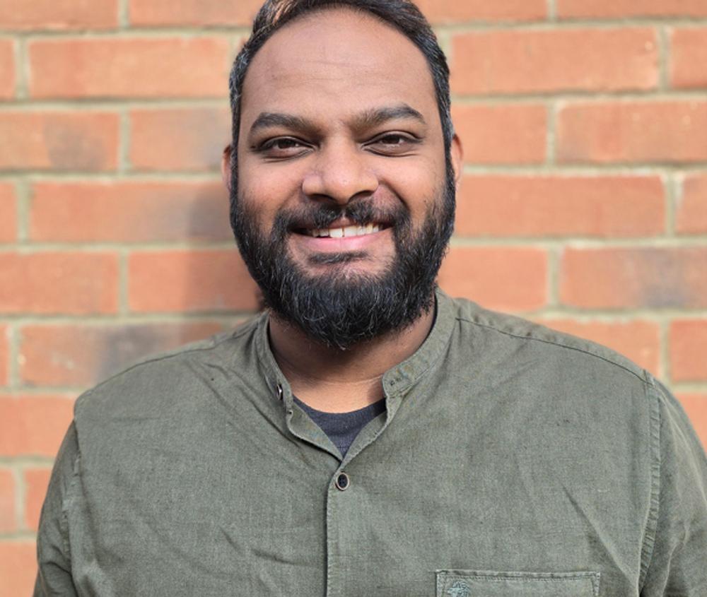 A portrait of Middlesex University graduate Hubert James standing in front of a brick wall