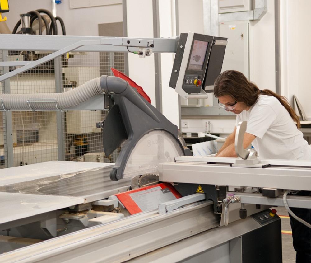 A female student leaning over a large machine in the MDX Design Engineering Lab