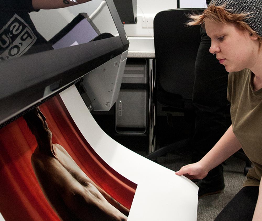 A student printing a large piece of paper with art work on it