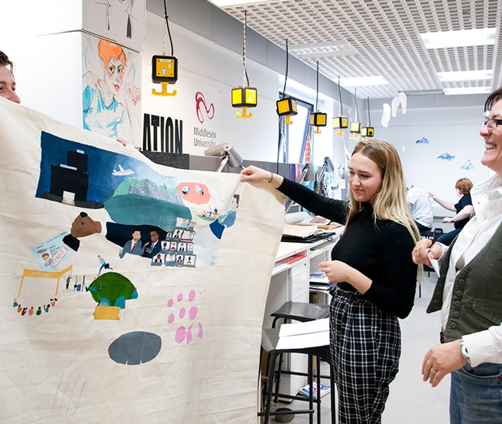 3 students looking a large piece of artwork smiling at it