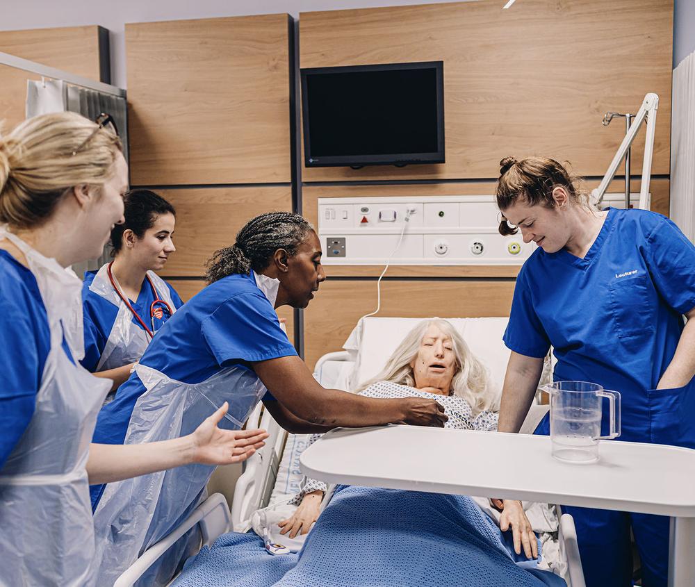 nurse demos procedure with dummy while student nurses watch on