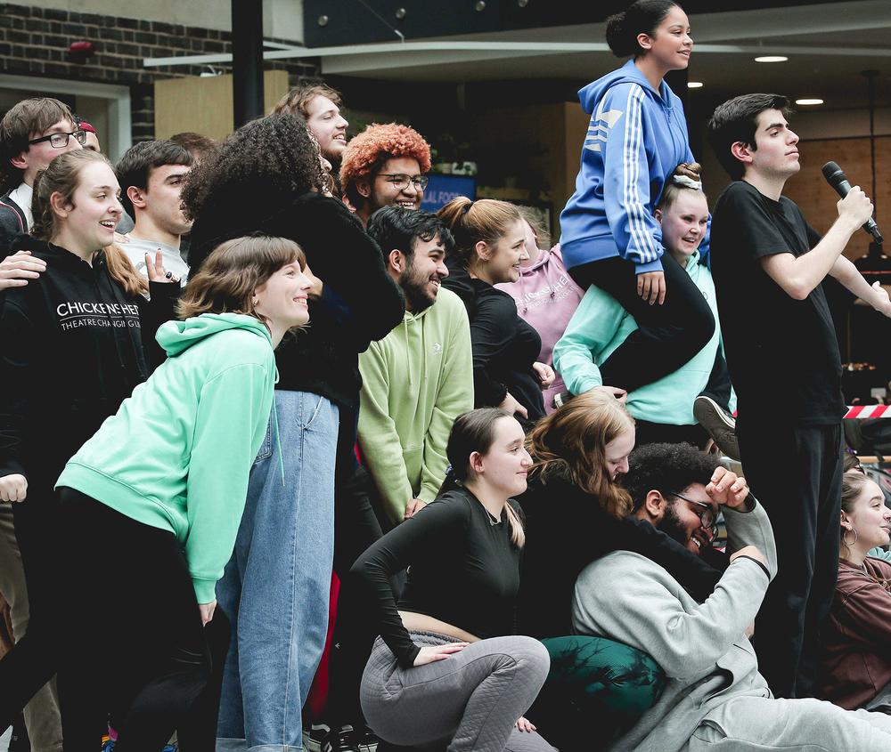 Large group of people posing behind performer with microphone