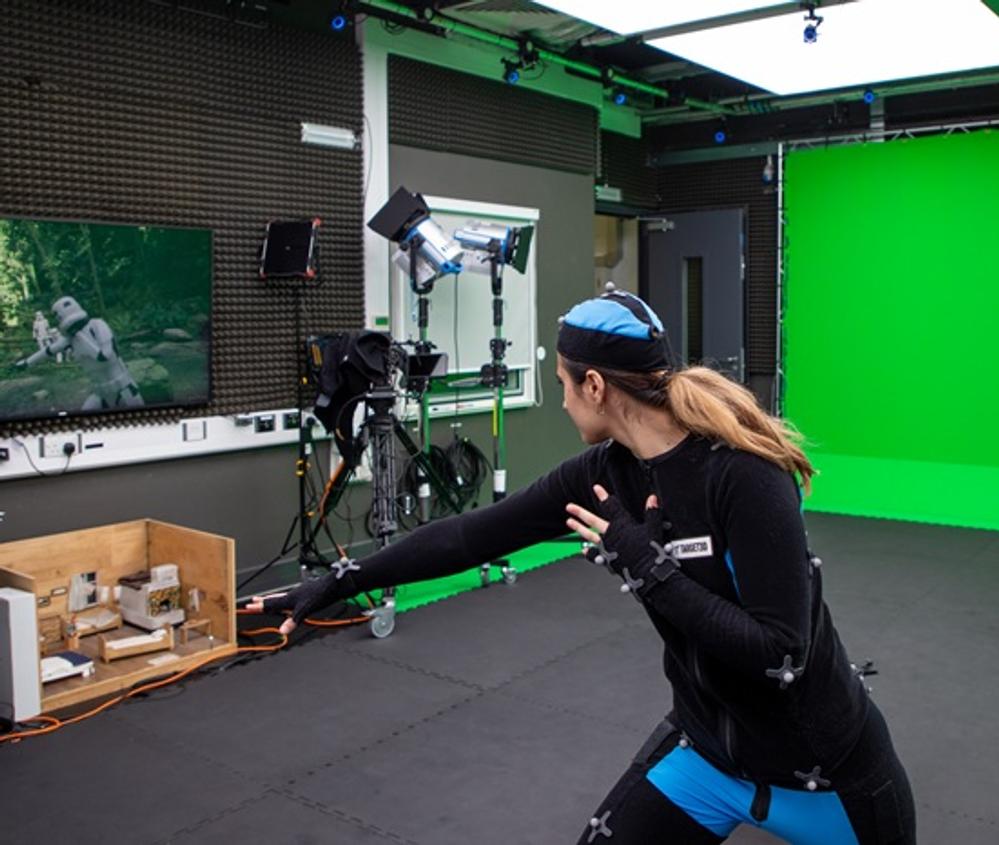A person in a motion capture suit pushing their fist forward, with an animated soldier on a screen emulating the action