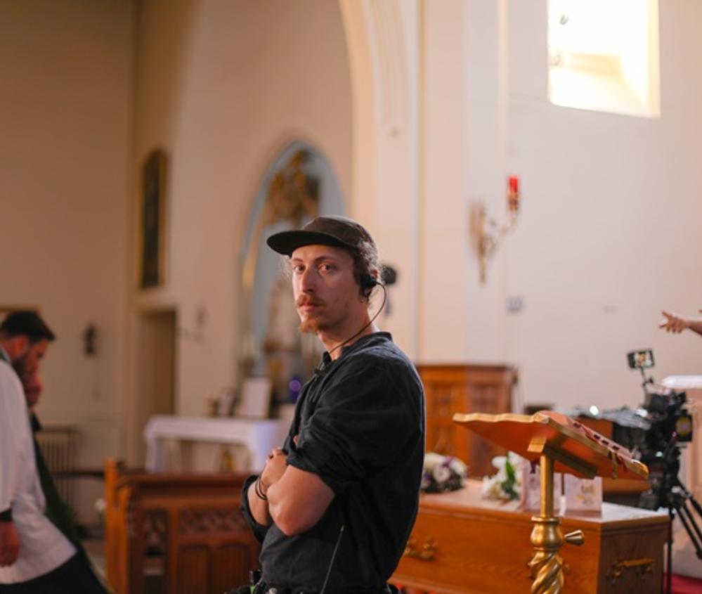 A production design student wearing black with earphones in, at a film set in a church