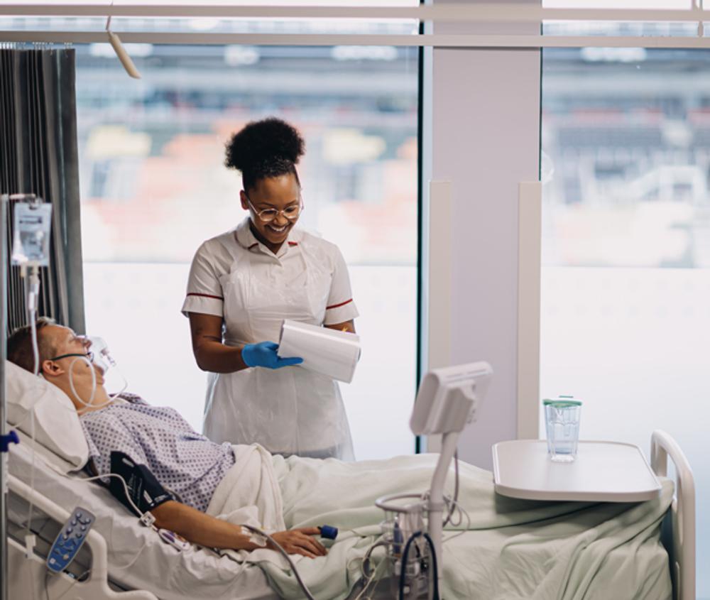 A student nurse talking to a patient in bed in a hospital ward