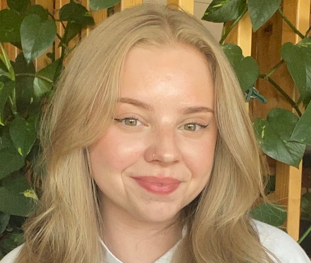 Wilma Claesson smiling while standing in front of a leafy plant
