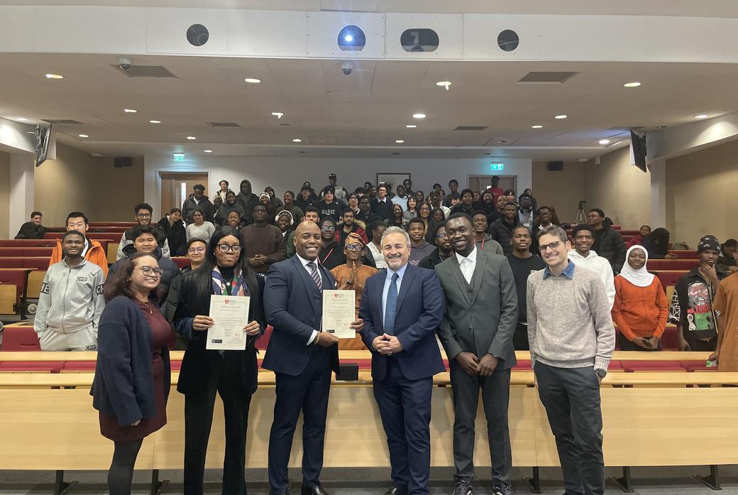A line-up of Computer Science lecturers and staff stand with two Nigerian visitors to Middlesex in a lecture theatre in Hatchcroft building