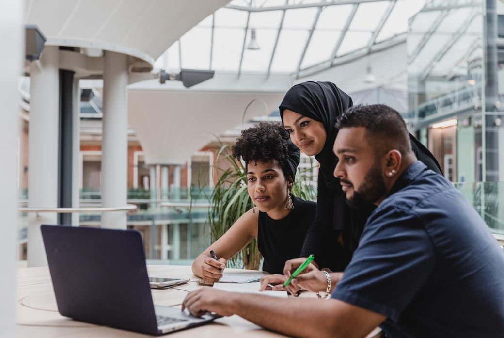 three people look at a laptop