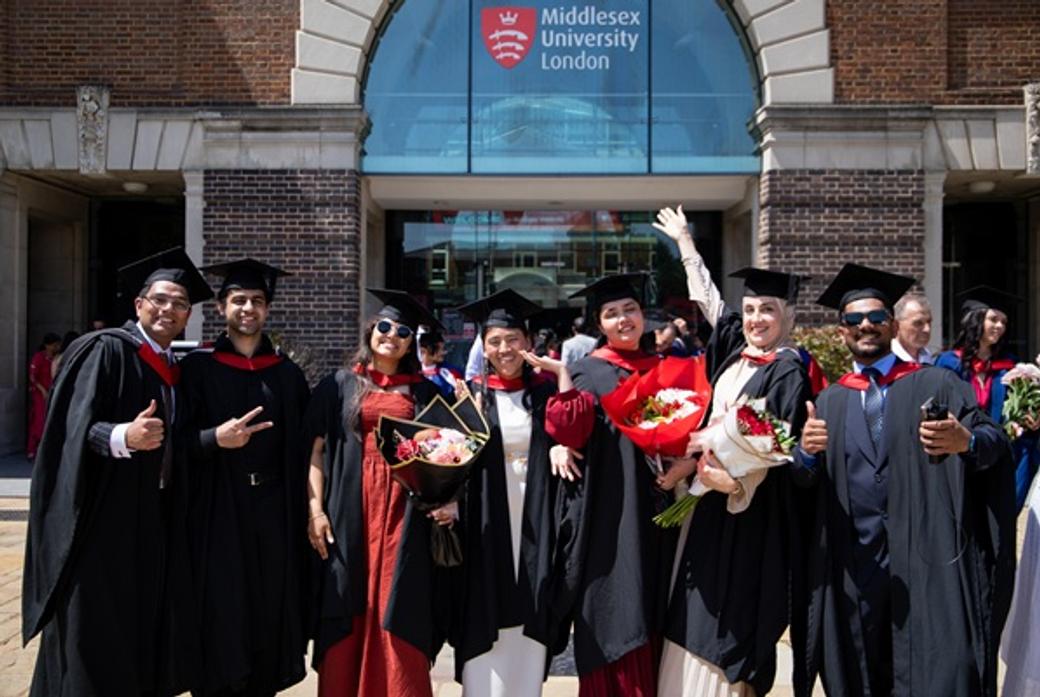 A group of enrobed graduates celebrating in front of the main Middlesex University London entrance