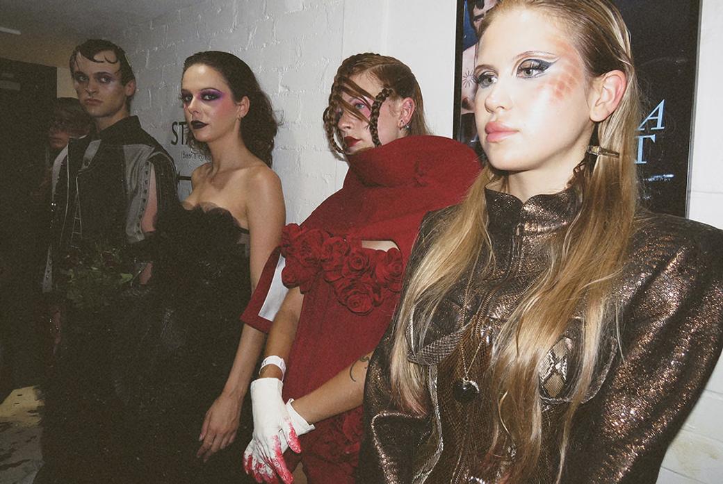 Three models stand together wearing pieces from a collection