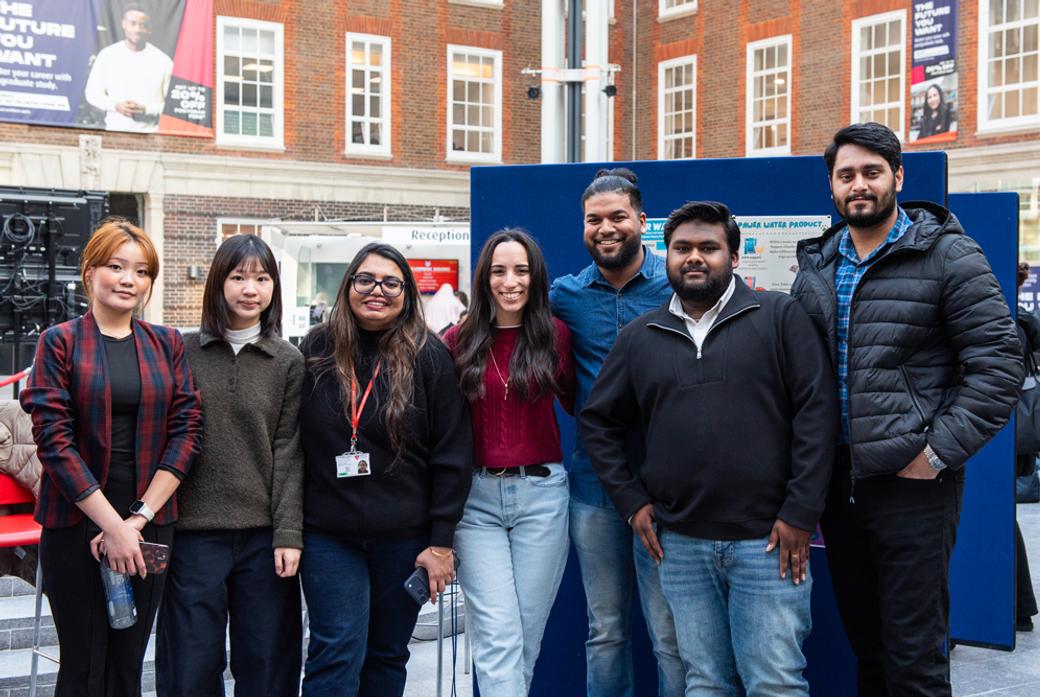 A group of students standing inside a university building, posing for the camera