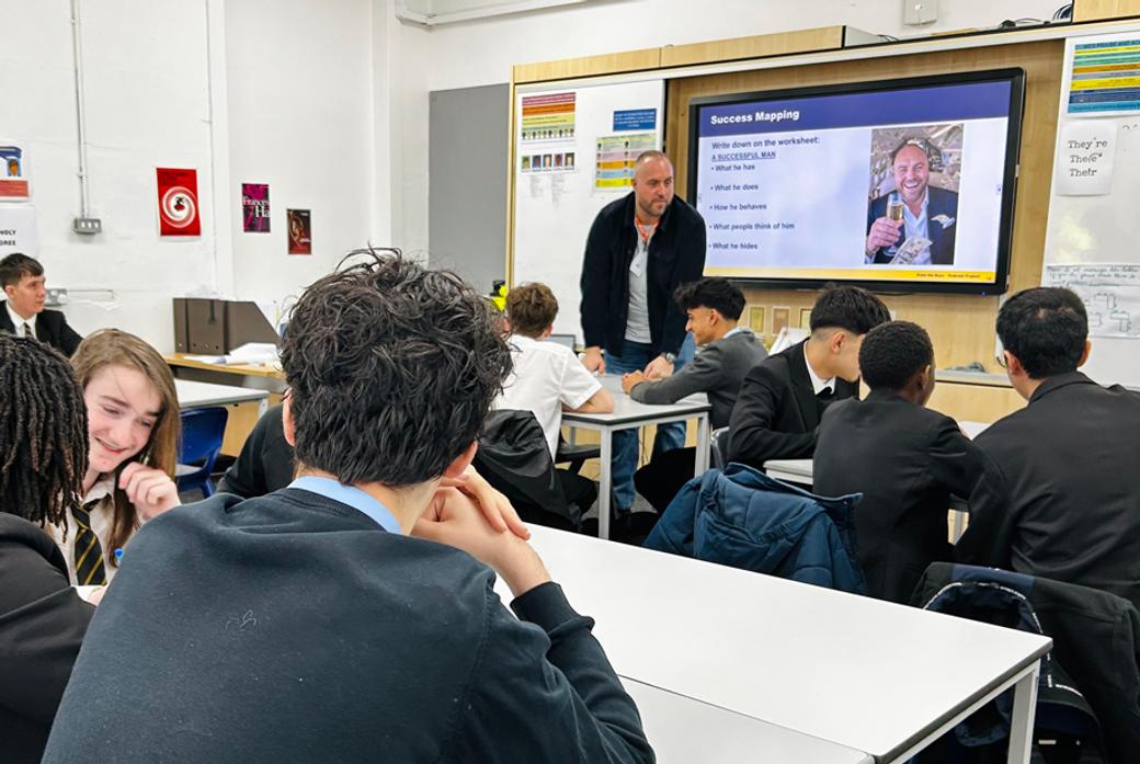 Male school pupils in a classroom watching an adult male standing up at a whiteboard