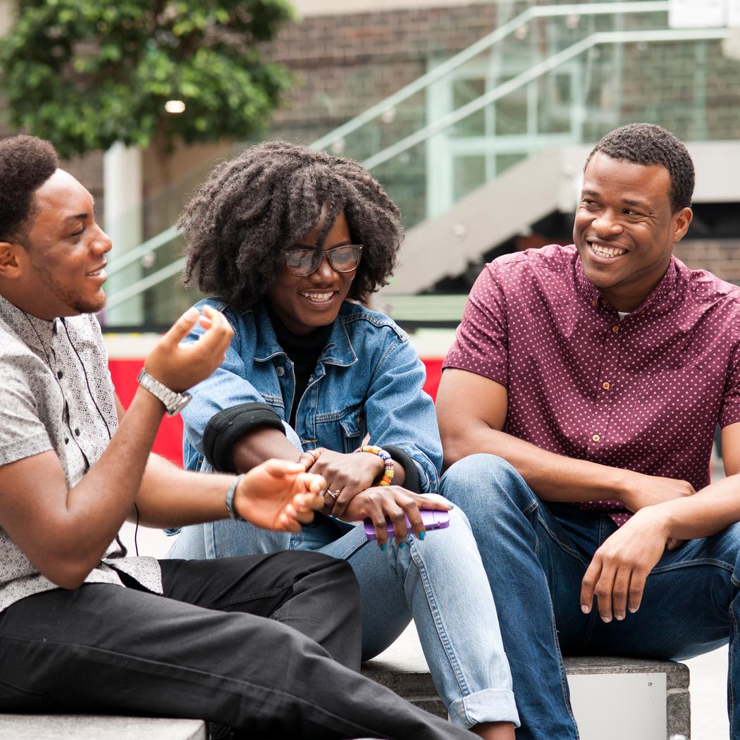 3 students sitting on a courtyard engaged in conversation