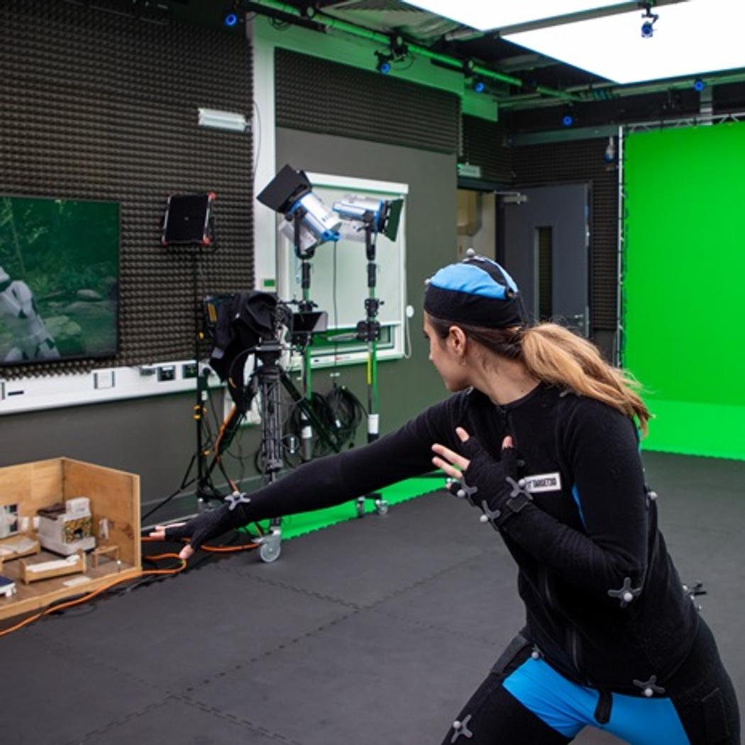 A person in a motion capture suit pushing their fist forward, with an animated soldier on a screen emulating the action