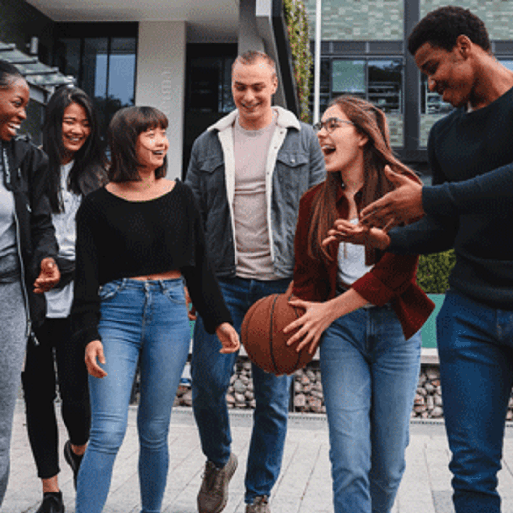 A diverse group of young adults walking together in a park, chatting and laughing, enjoying each other's company.