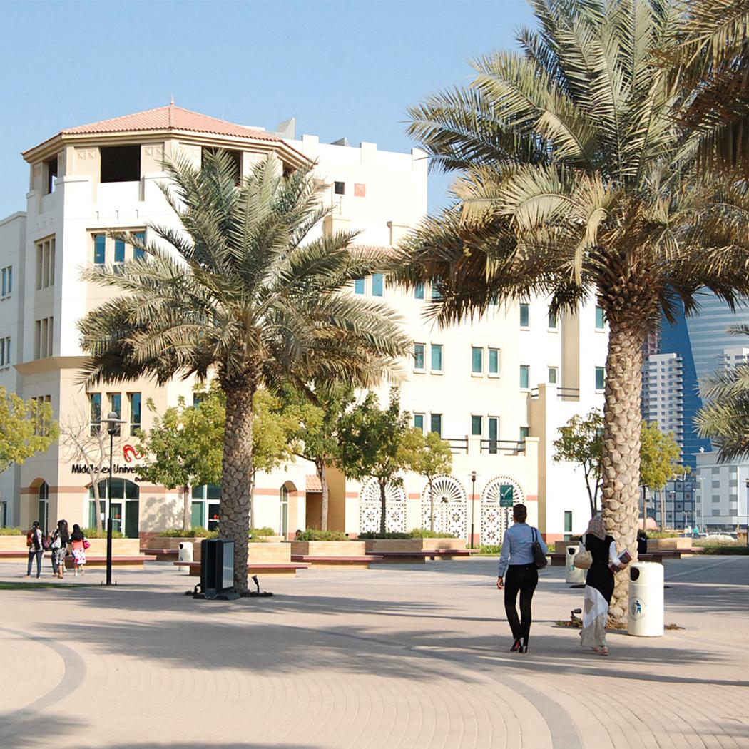 students walking along a street with dubai campus and palm trees in the background