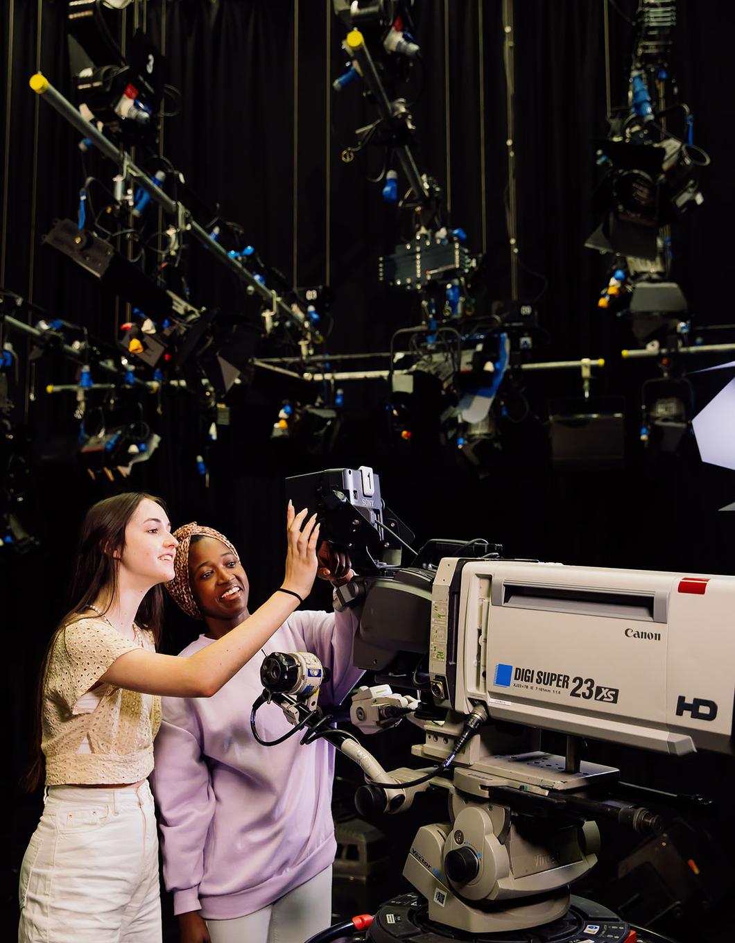 two students in a large dark studio looking into display of large camera