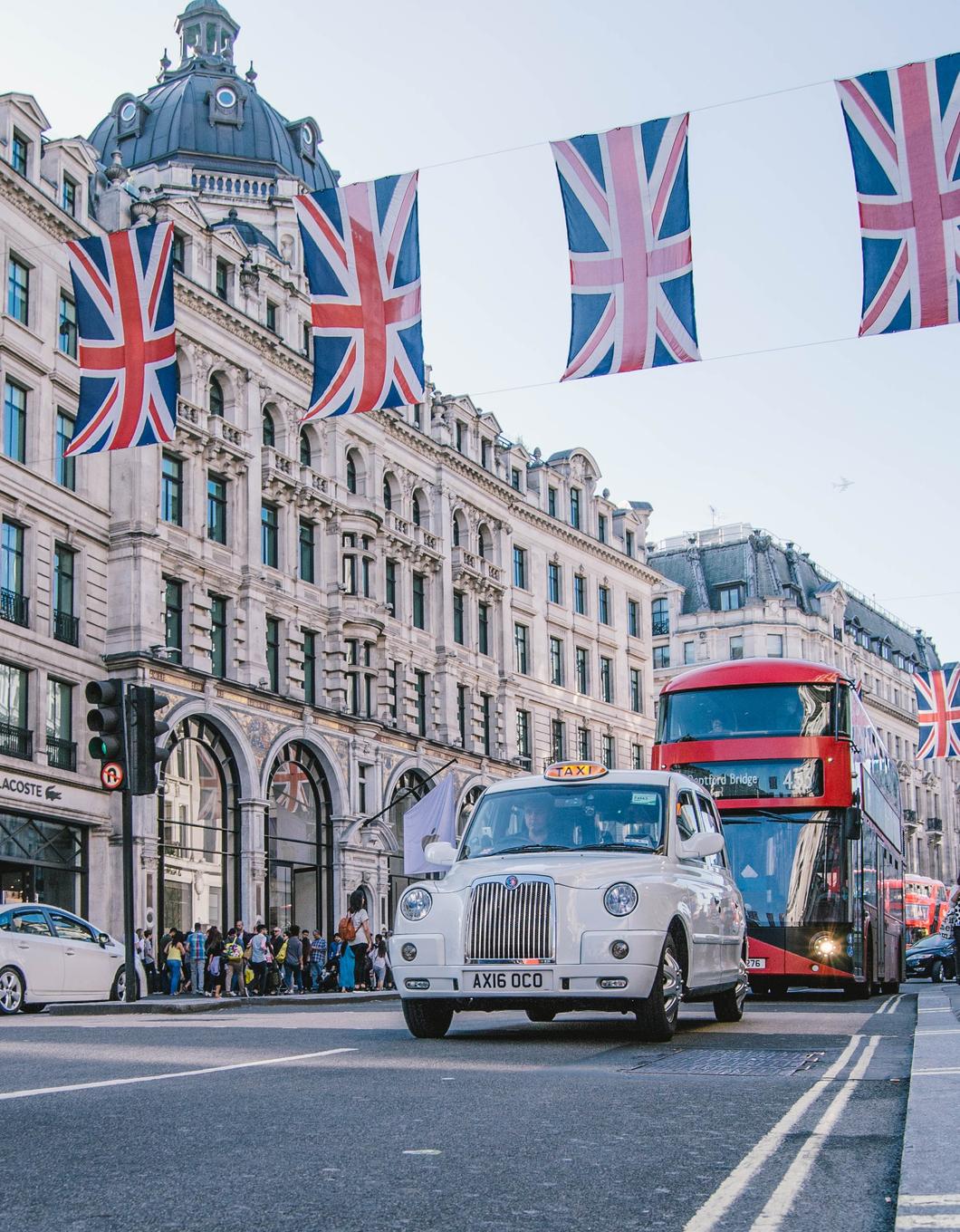 A white car driving down a street lined with British flags.