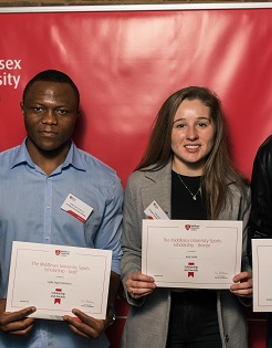 Four individuals proudly displaying certificates in front of a vibrant red wall.