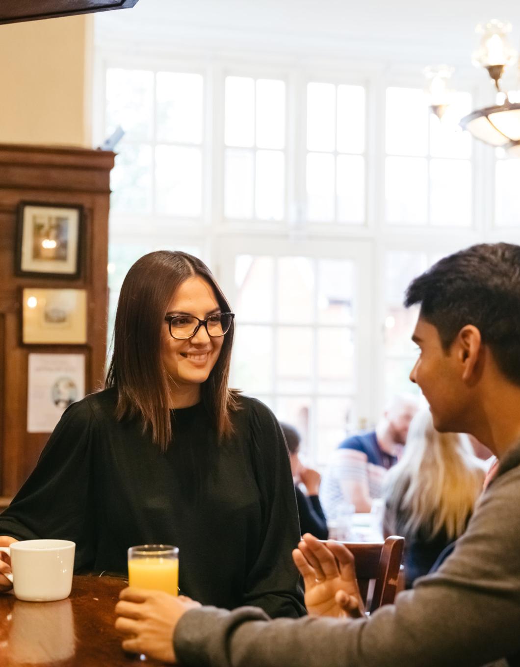 A couple enjoying a meal together at a restaurant, engaged in conversation and smiling at each other.