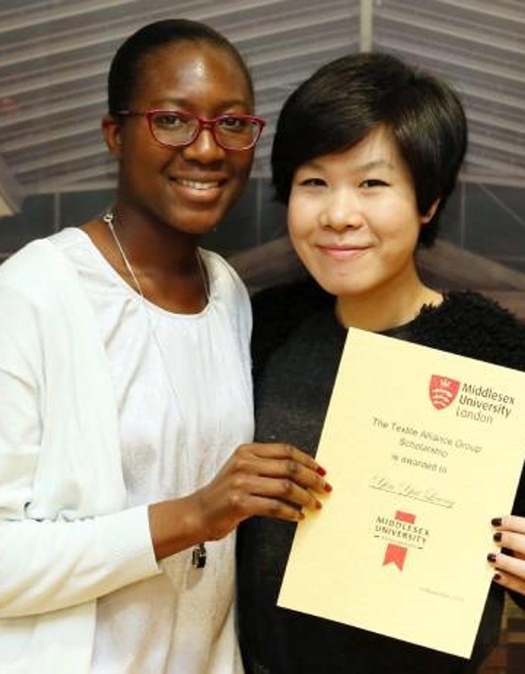 Two women proudly displaying a certificate in front of a building, symbolizing their achievement.