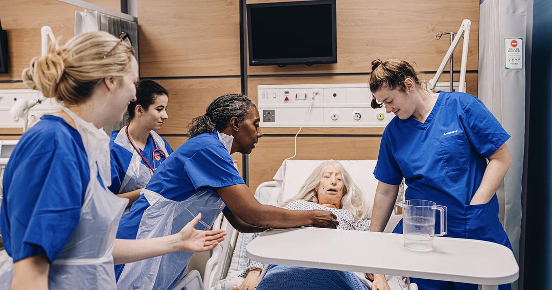 nurse demos procedure with dummy while student nurses watch on
