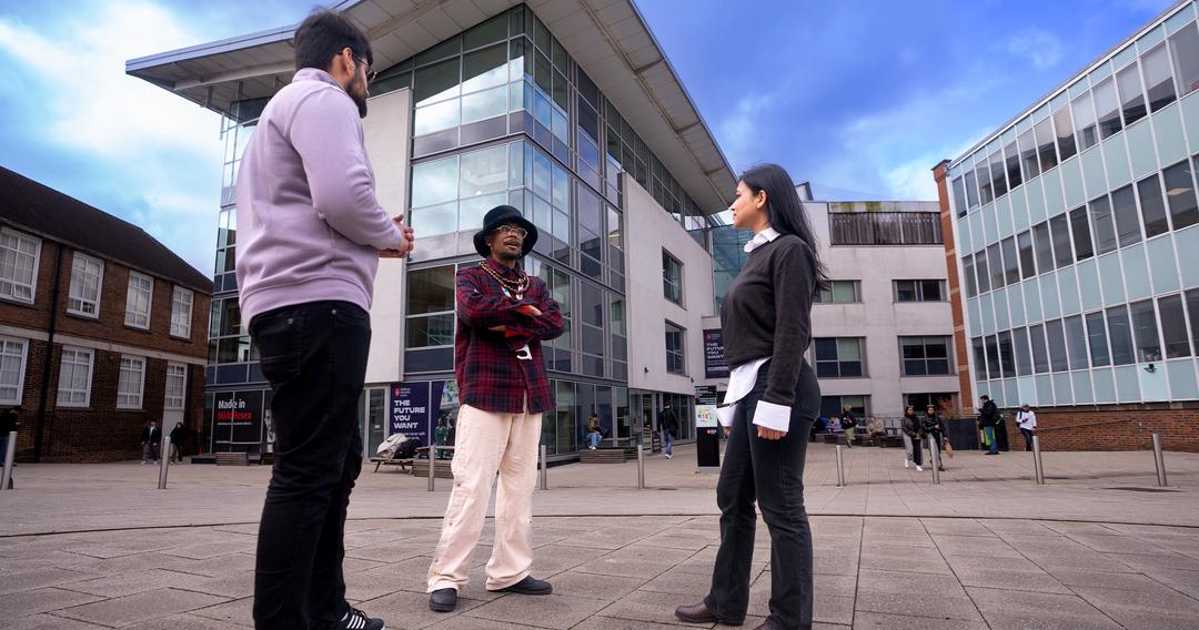 Three Middlesex students standing outside campus buildings with blue sky behind.