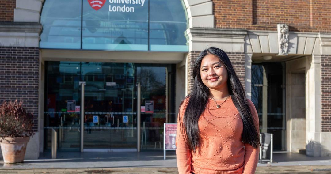 Smiling female student in front of a red brick building reading middlesex university