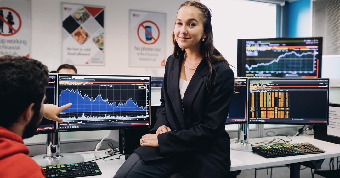 Student sitting on a desk with screen behind displaying a graph.