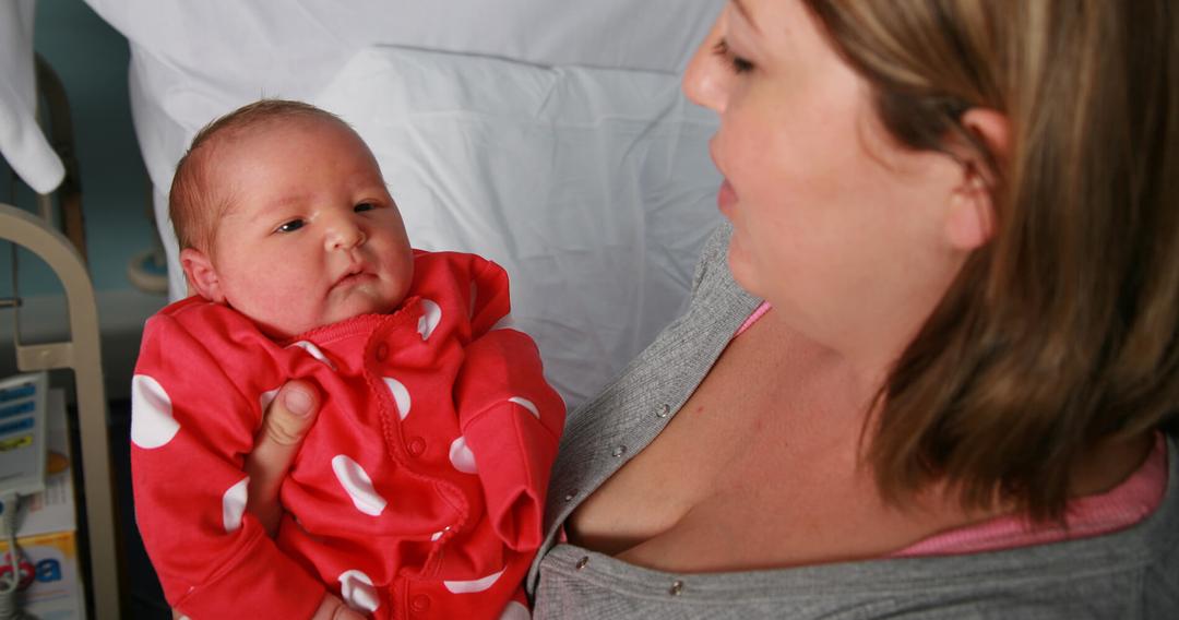 Mother holding baby in red spotted baby grow