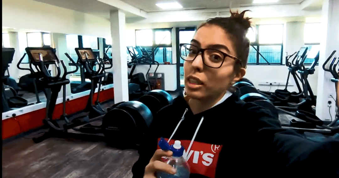 international student in the gym holding a water bottle and wearing glasses