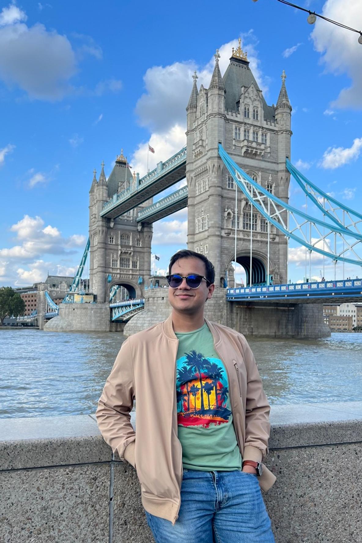 A man leaning against a wall at the Thames with Tower Bridge in the background