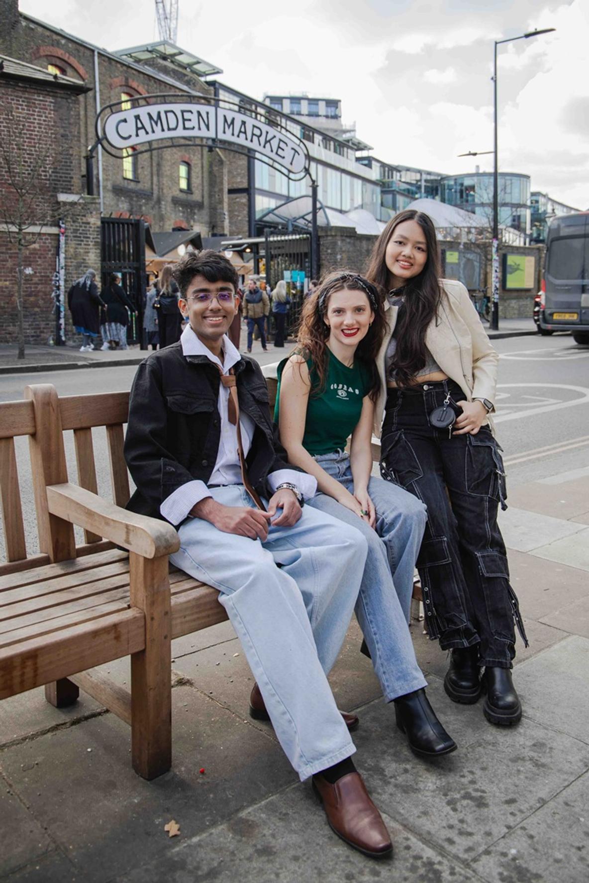 Three students smiling on a bench outside a sign for Camden Market