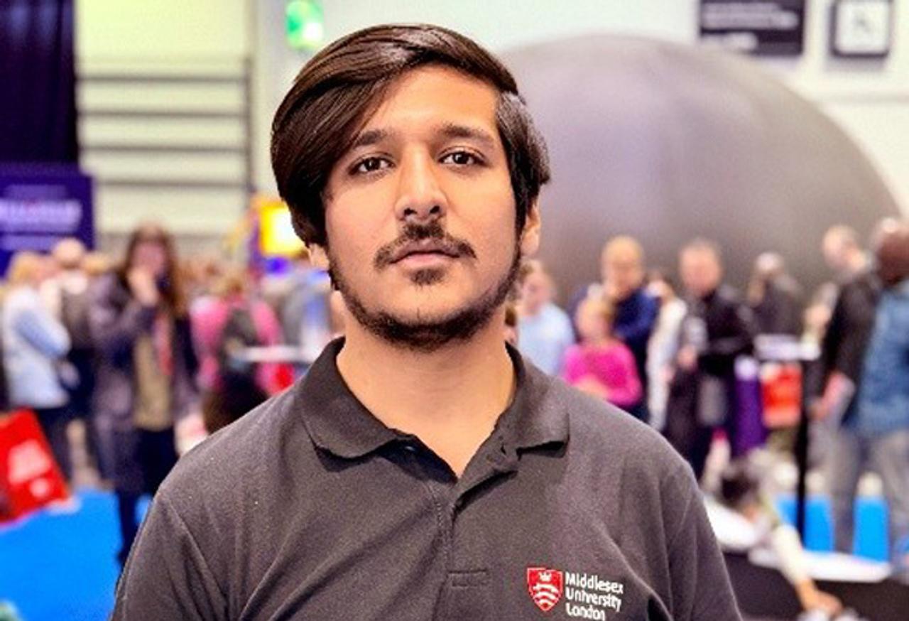 A young man standing in an exhibition looking at the camera