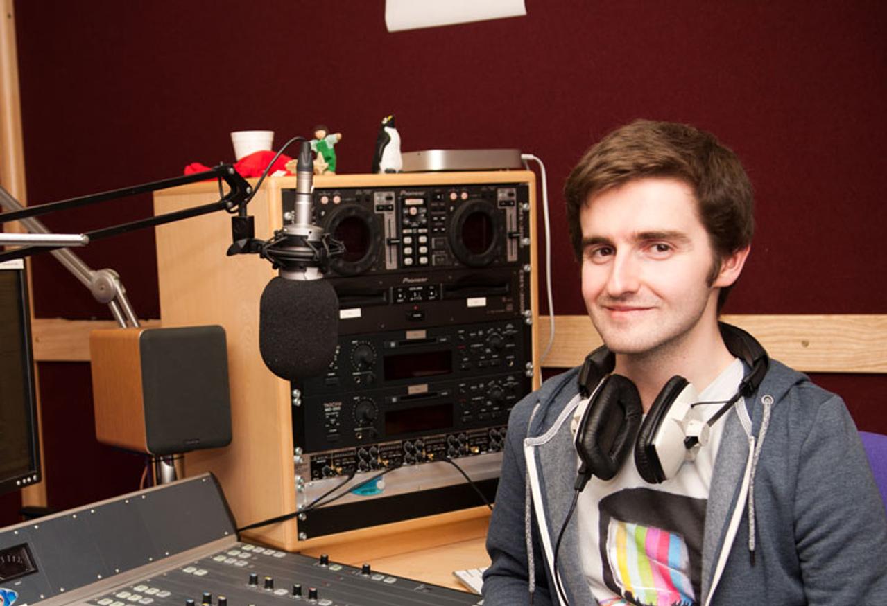 Male student wearing headphones sitting in front of a music mixer device