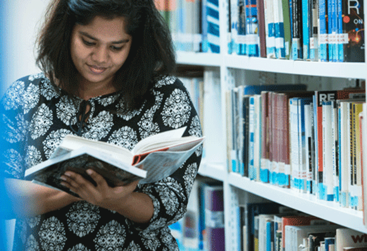 A woman engrossed in reading a book amidst the serene ambiance of a library.