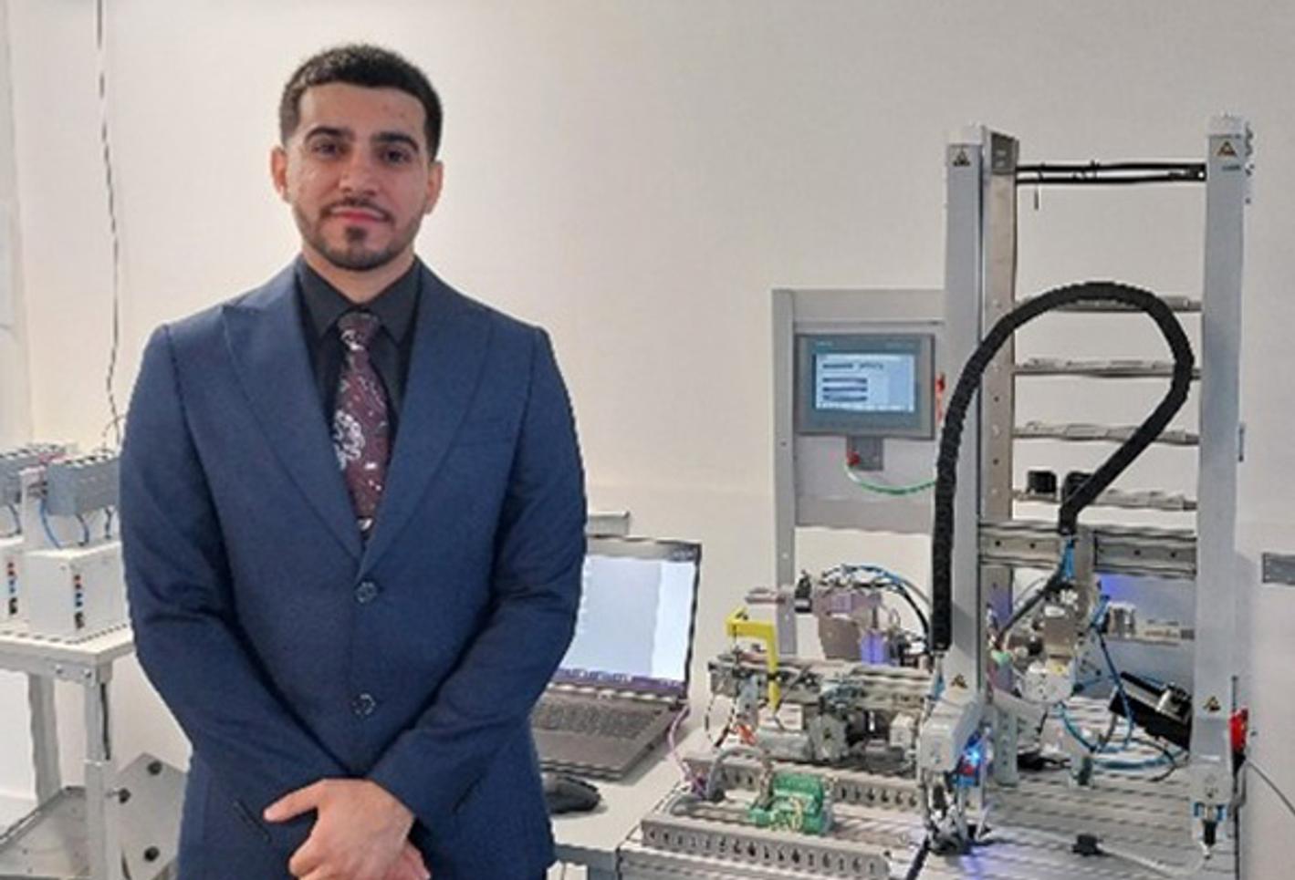 A man in a suit standing in front of mechatronics equipment looking at the camera