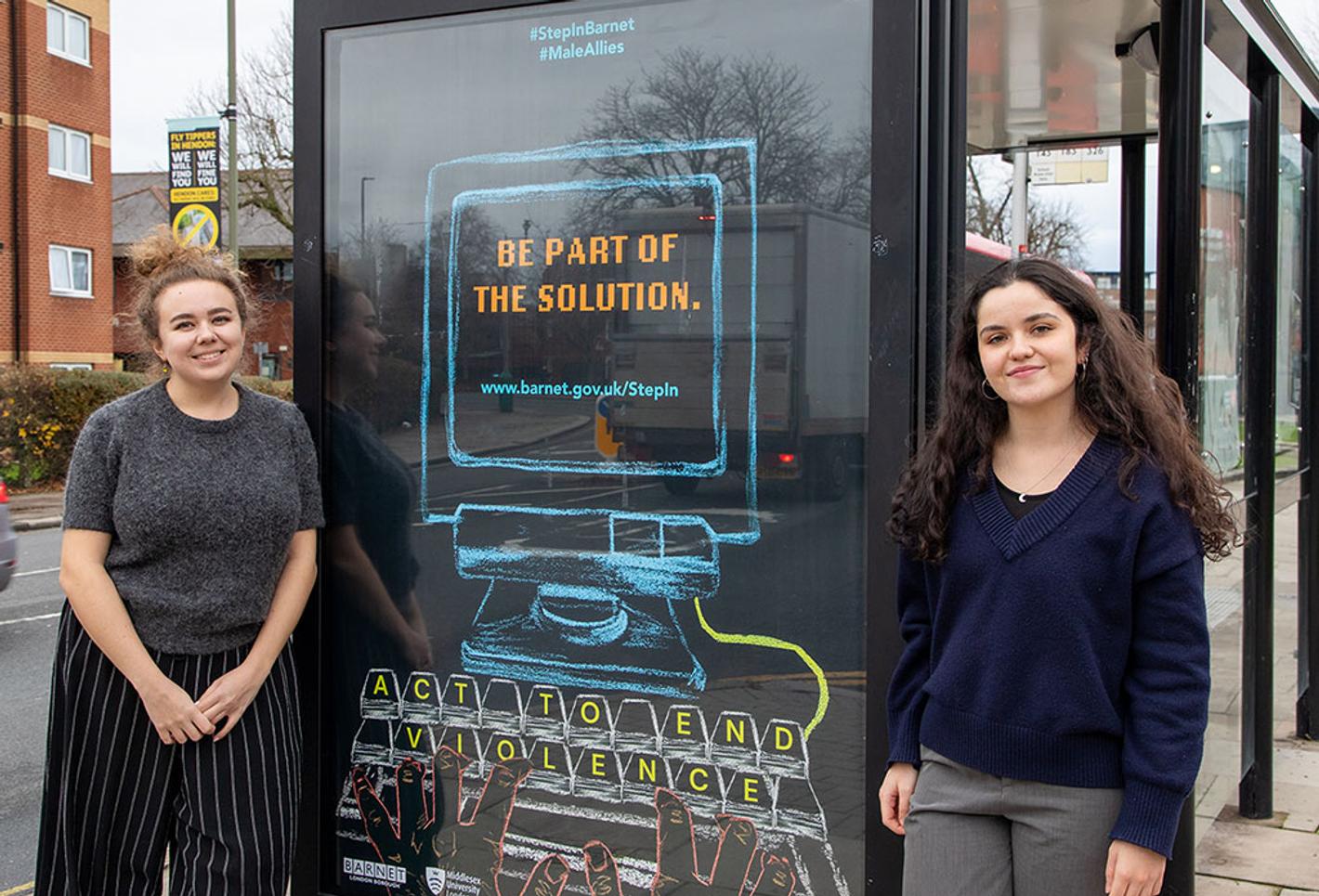 Two students stand either side of a bus stop showing their campaign poster