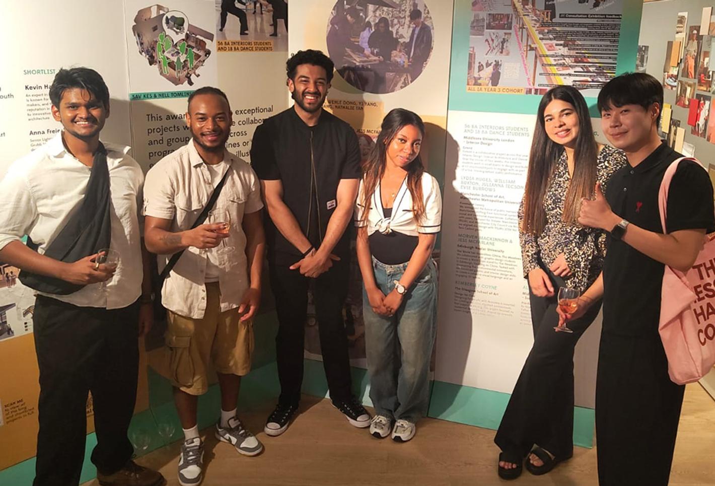 Students stand in front of posters of their designs that won awards.