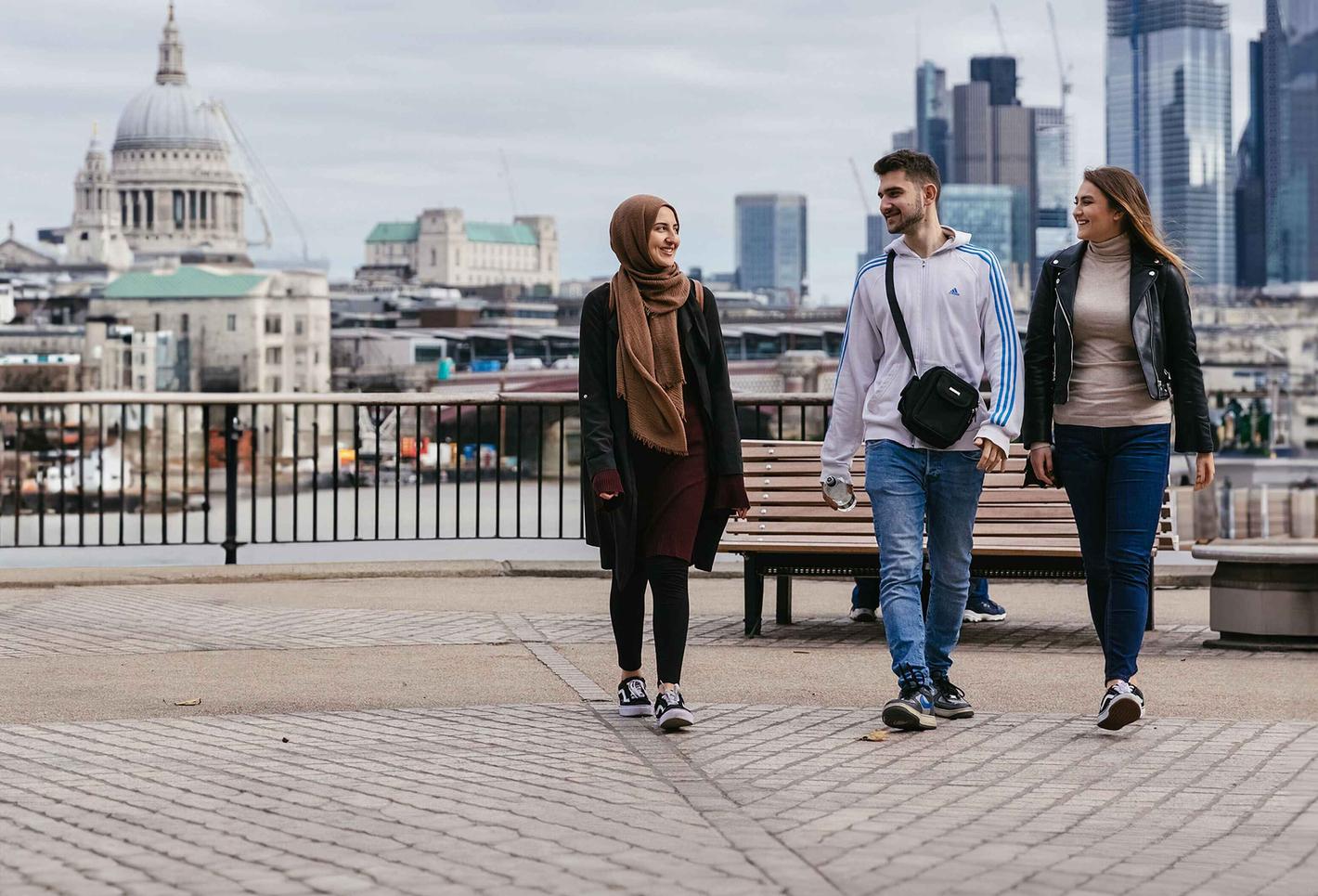 3 middlesex university students walk along the thames with st pauls in the background