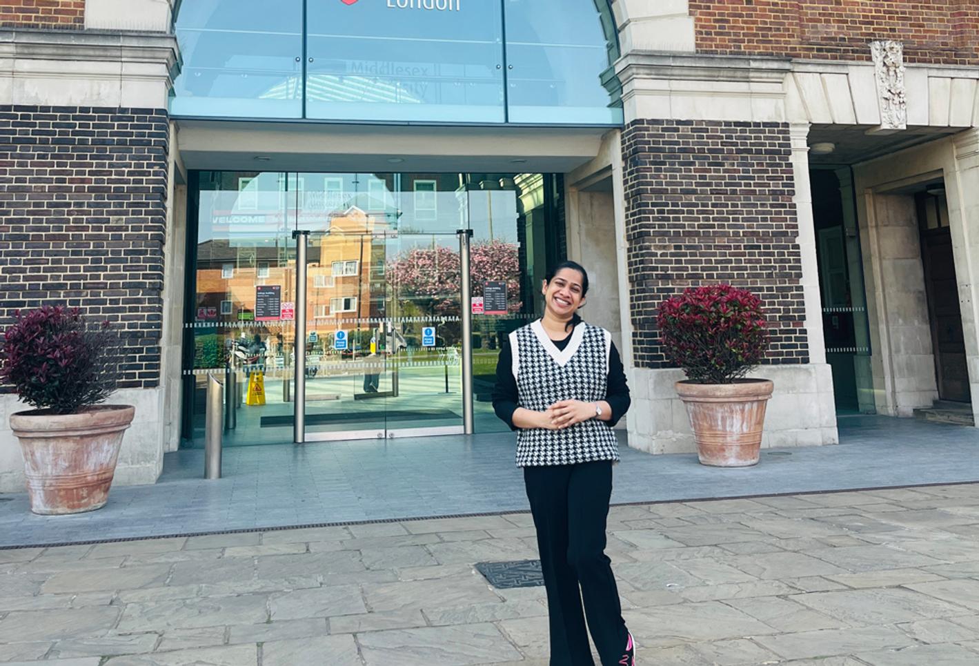A woman stands in front of the entrance to a university building