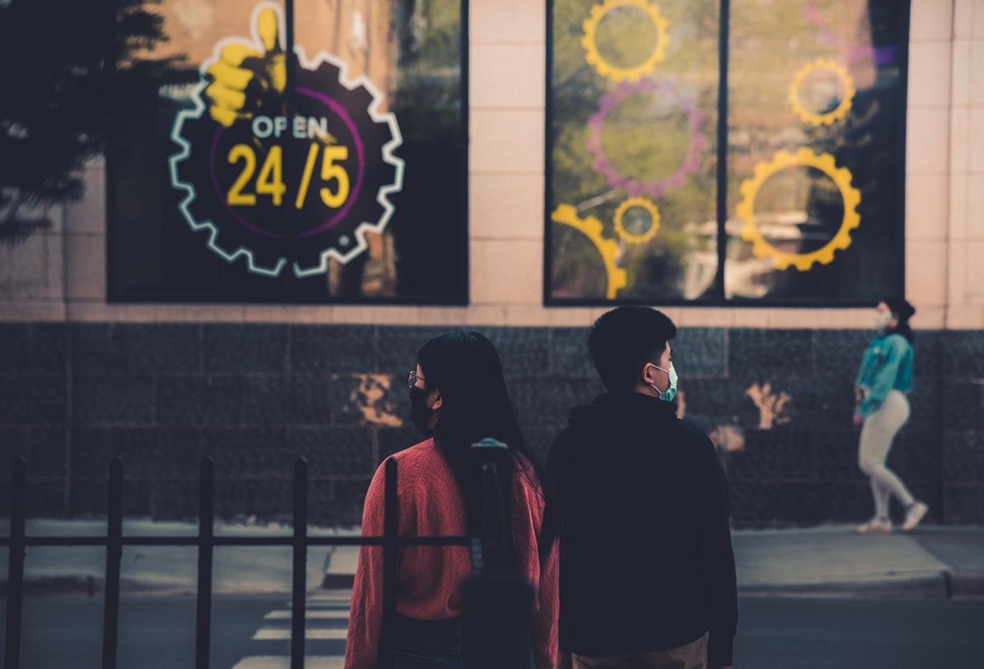 Two individuals standing in front of a building wearing face mask