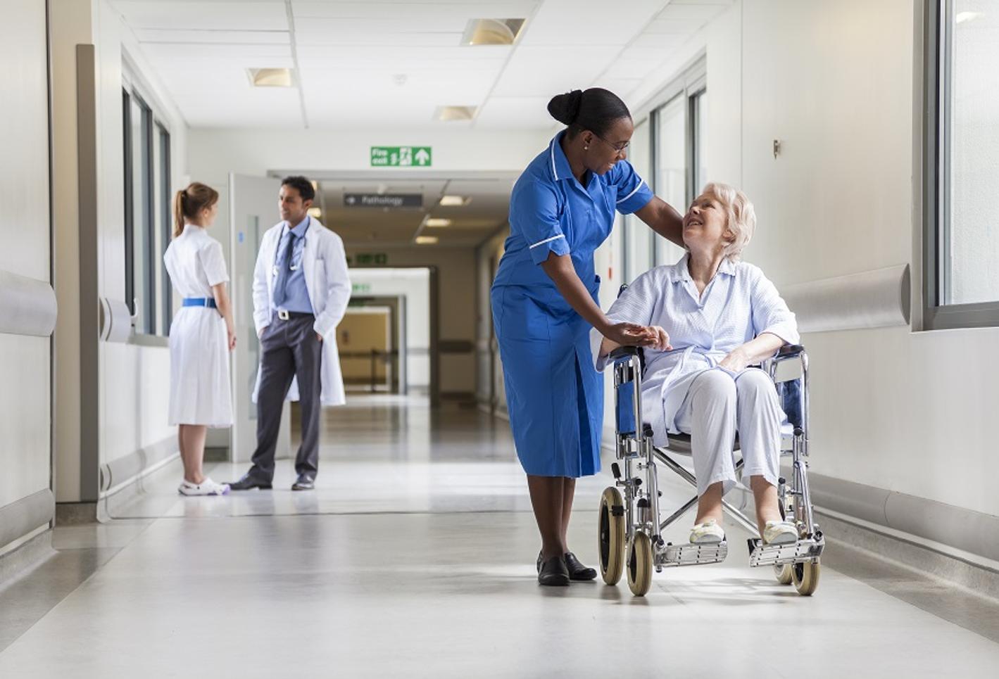 A caring nurse assisting an elderly woman in a wheelchair in a hospital corridor.