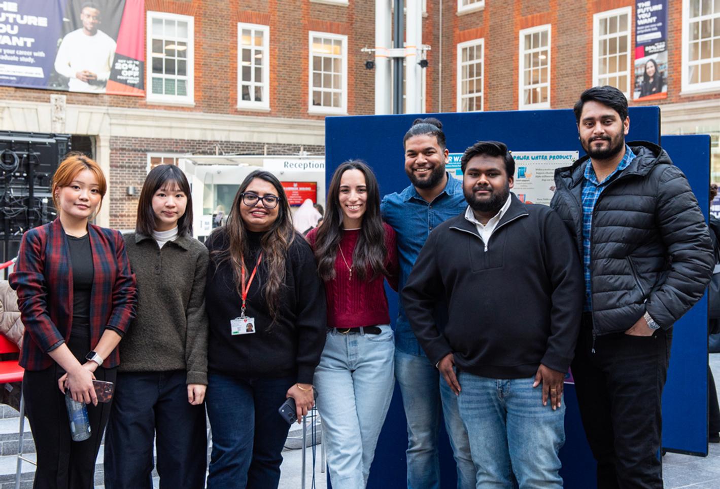 A group of students standing inside a university building, posing for the camera