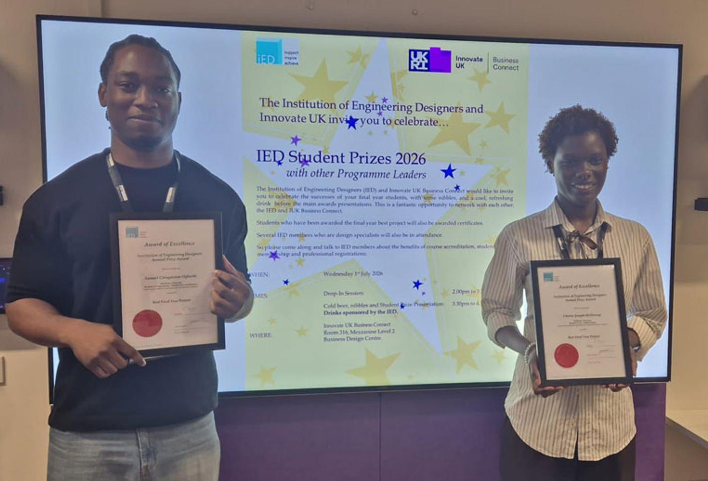 Two award winners holding certificates, with a screen behind them displaying their prize.