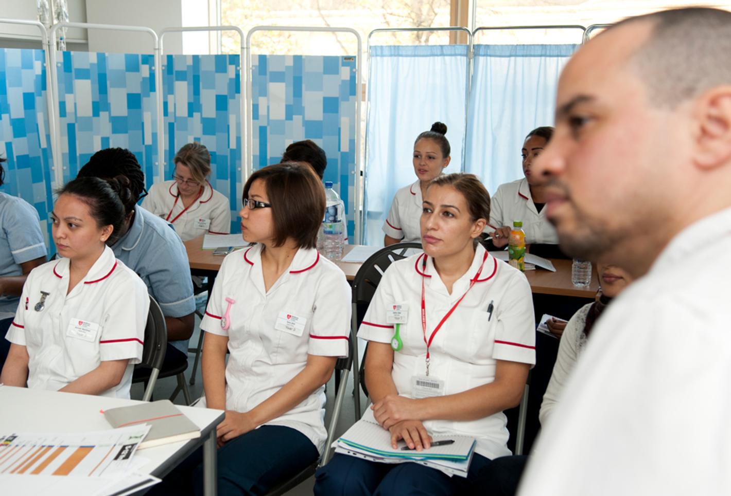 A group of trainee healthcare workers sitting in a practice ward listening to a training session