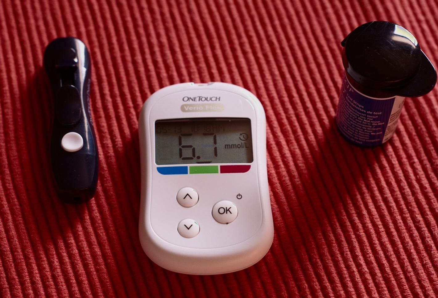 Image of a digital blood glucose meter next to a bottle of lancets and a lancet for blood sugar testing.