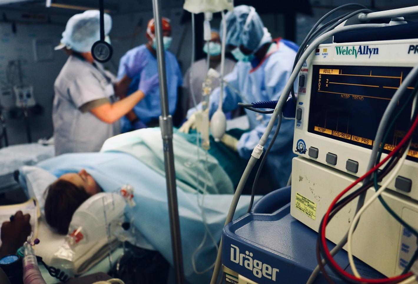 A hospital room with a patient lying on a bed, surrounded by medical personnel and equipment