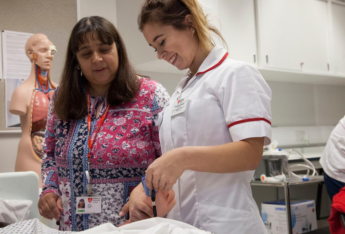 Two nurses assisting a baby in a hospital room.