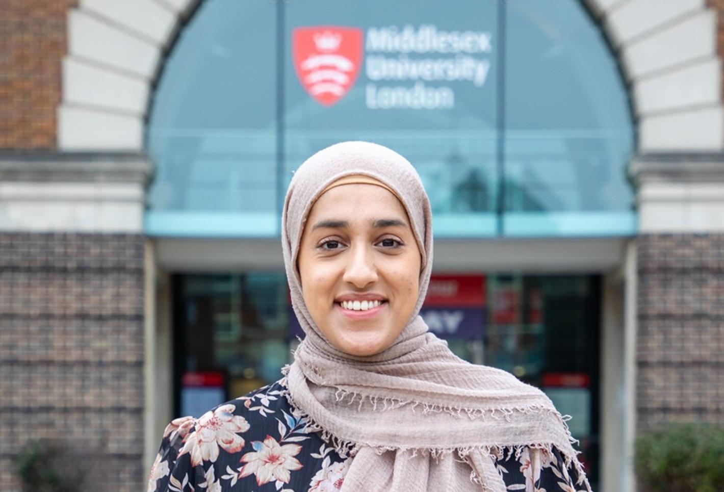 Aqsa Rabbani standing and smiling in front of the entrance to Middlesex University's College Building
